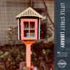 Handcrafted little street library in front of a charming cottage style home with garden
